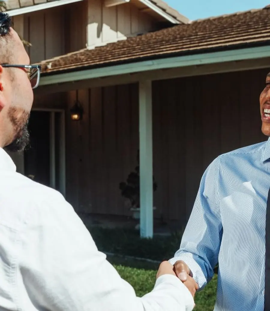 Real estate agent shaking hands with a client in front of a home